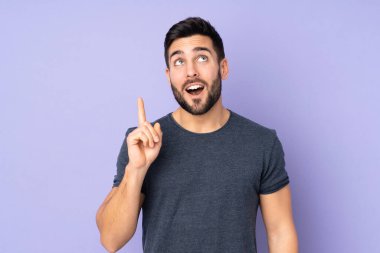 Kafkasyalı yakışıklı bir adam, izole edilmiş mor arka plan üzerinde parmağı gösteren bir fikir düşünüyor.