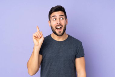 Kafkasyalı yakışıklı adam çözümü kavramak için parmağını izole edilmiş mor arka plan üzerine kaldırıyor.