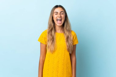 İzole edilmiş mavi arka planda, ağzı açık bir şekilde bağıran genç İspanyol kadın.