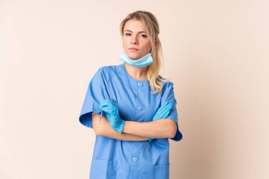 Arkaplanda aletleri tutan dişçi kadın kollarını çapraz tutuyor.