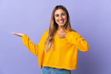 İzole edilmiş mor arkaplan üzerine genç İspanyol kadın bir ilan vermek ve onaylamak için avucunun içinde hayali bir şey tutuyor.