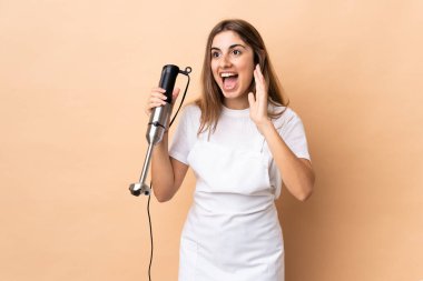 El blenderi kullanan bir kadın, izole edilmiş bir arkaplanda yüz ifadesini şaşırtıyor.