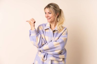 İzole edilmiş arka planda sarışın bir kadın bir ürün sunmak için kenarı işaret ediyor.