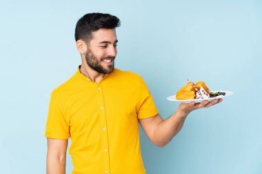 Mavi arka planda mutlu bir ifadeyle izole edilmiş waffle tutan beyaz bir adam.