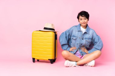 Genç gezgin Vietnamlı bavullu kadın arka planda izole edilmiş pembe arka planda oturuyor.