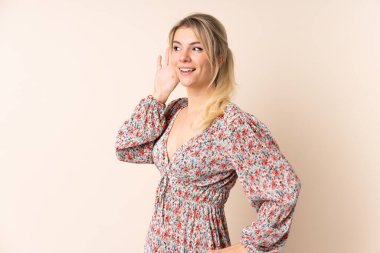 Sarışın kadın, izole edilmiş arka planda bir şey dinlerken elini kulağına koyar.