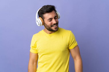Mor arka planda izole edilmiş sakallı yakışıklı genç adam müzik dinliyor.