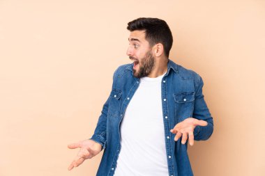 Beyaz tenli yakışıklı, bej arka planda izole edilmiş, sürpriz bir ifadeyle yan yana bakarken.