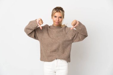 Beyaz arka planda izole edilmiş genç bir Rus kadın baş parmağını iki eliyle aşağı gösteriyor.