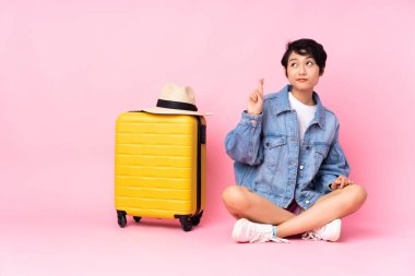 Genç gezgin Vietnamlı bavullu kadın izole pembe arka planda oturuyor ve dua ediyor.
