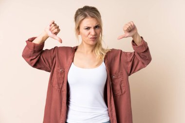 Sarışın kadın, izole edilmiş arka planda baş parmağını iki eliyle gösteriyor.