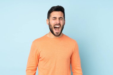Kafkasyalı yakışıklı adam ön tarafa bağırıyor, ağzı sonuna kadar açık, izole edilmiş mavi arka planda.