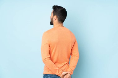 Beyaz tenli yakışıklı adam arka planda ve izole edilmiş mavi arka plana bakıyor.