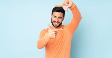 Yüzüne odaklanan beyaz, yakışıklı bir adam. İzole edilmiş mavi arkaplan üzerindeki çerçeve sembolü