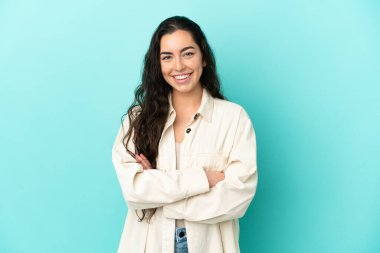 Mavi arka planda izole genç beyaz kadın kollarını ön cephede çapraz tutuyor.