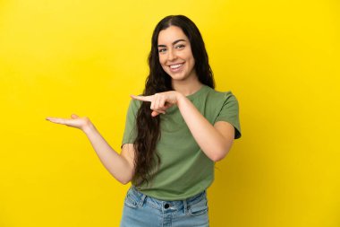 Sarı arka planda izole edilmiş genç beyaz kadın bir ilan vermek için avucunun içinde hayali bir mekan tutuyor.