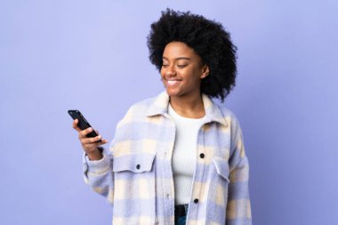 Mor arka planda izole edilmiş, mutlu bir ifadeyle cep telefonu kullanan genç Afrikalı Amerikalı kadın.