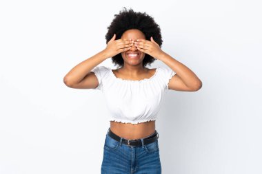 Beyaz arka planda izole edilmiş genç Afrikalı Amerikalı bir kadın. Gözleri elleriyle kaplıyor ve gülümsüyor.