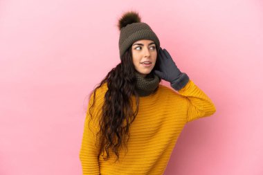 Mor arka planda izole edilmiş beyaz şapkalı genç bir kız elini kulağına koyarak bir şeyler dinliyor.