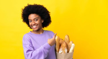 Genç Afrikalı Amerikalı bir kadın sarı arka planda izole edilmiş bir ekmek alıyor.