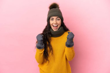 Mor arka planda izole edilmiş, kazanan pozisyondaki zaferi kutlayan, kışlık şapkalı beyaz bir kız.