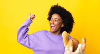 Genç Afrikalı Amerikalı bir kadın sarı arka planda izole edilmiş bir ekmek alıyor ve zaferi kutluyor.