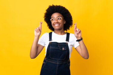 Sarı arka planda izole edilmiş genç Afrikalı Amerikalı kadın parmaklarını çapraz yapıp en iyisini diliyor.