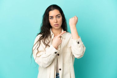 Mavi arka planda izole edilmiş beyaz bir kadın geç kalma jesti yapıyor.