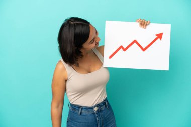 Mavi arka planda izole edilmiş genç melez bir kadın elinde büyüyen bir istatistik okuyla mutlu bir ifadeyle bir işaret tutuyor.