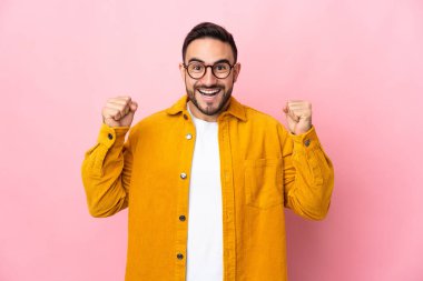 Pembe arka planda izole edilmiş beyaz, yakışıklı genç bir adam galibiyeti kutluyor.