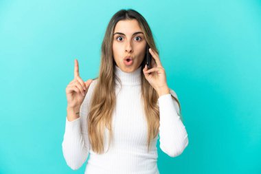 Mavi arka planda izole edilmiş cep telefonu kullanan genç beyaz kadın bir fikri işaret ederek...