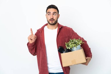 Beyaz arka planda izole edilmiş şeylerle dolu bir kutuyu kaldırırken genç beyaz bir adam hareket ediyor.