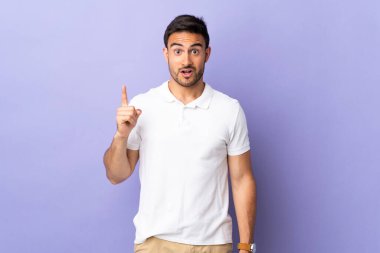 Mor arka planda izole edilmiş genç yakışıklı bir adam parmağını kaldırarak çözümü anlamaya çalışıyor.