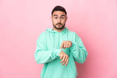 Pembe arka planda izole edilmiş beyaz, yakışıklı bir adam geç kalma jesti yapıyor.