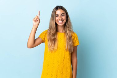 İzole edilmiş mavi arka planda genç İspanyol kadın harika bir fikre işaret ediyor.