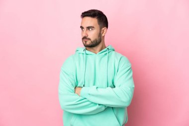 Pembe arka planda izole edilmiş beyaz, yakışıklı genç bir adam kollarını kavuşturuyor.