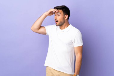 Mor arka planda soyutlanmış genç yakışıklı bir adam yan tarafa bakarken sürpriz jest yapıyor.