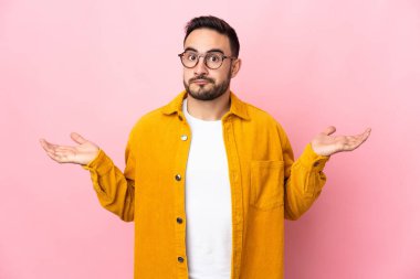 Pembe arka planda soyutlanmış beyaz, yakışıklı genç adam ellerini kaldırırken şüphe duyuyor.