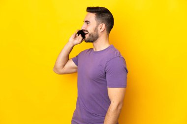 Sarı arka planda izole genç beyaz yakışıklı adam cep telefonuyla sohbet ediyor.