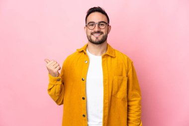 Pembe arka planda izole edilmiş beyaz, yakışıklı genç bir adam bir ürün sunmak için kenarı işaret ediyor.