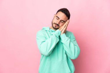 Pembe arka planda izole edilmiş beyaz, yakışıklı genç bir adam uyku jesti yapıyor.