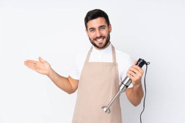 Beyaz arka planda izole edilmiş el blenderi kullanan adam davet edilmek için ellerini yana uzatıyor