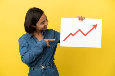 Sarı arka planda izole edilmiş genç melez bir kadın. Elinde büyüyen bir istatistik okunun sembolü olan bir tabela tutuyor ve işaret ediyor.