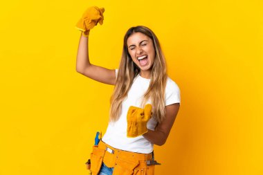 Genç İspanyol elektrikçi kadın izole edilmiş sarı duvarda zaferi kutluyor.