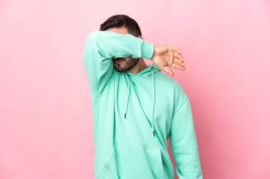 Beyaz tenli yakışıklı, pembe arka planda izole edilmiş, gözleri elle kaplanmış.