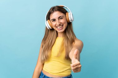 Soyutlanmış mavi arka planda müzik dinleyen genç bir kadın.