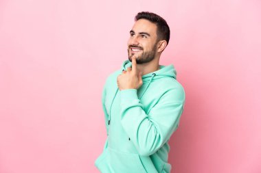 Beyaz tenli yakışıklı adam pembe arka planda izole edilmiş gülümserken yukarı bakıyor.