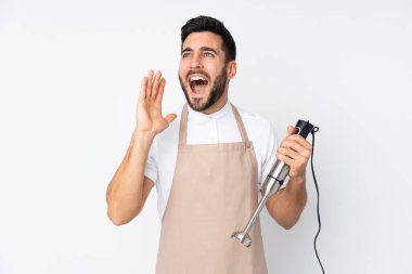 Beyaz arka planda izole edilmiş el blenderi kullanan adam ağzı açık bağırıyor.