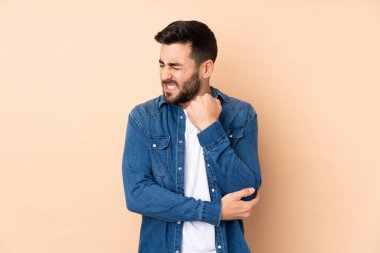 Beyaz tenli yakışıklı adam bej arka planda izole edilmiş, dirsek ağrısı var.