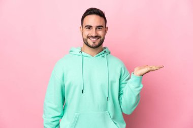 Beyaz tenli yakışıklı, pembe arka planda izole edilmiş. Avucunun içinde hayali bir ilan tutuyor.